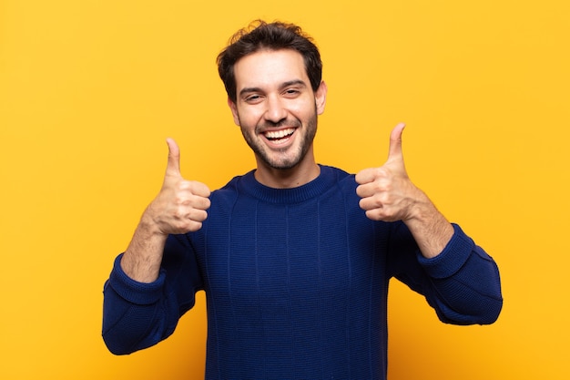 Young handsome man smiling broadly looking happy, positive, confident and successful, with both thumbs up