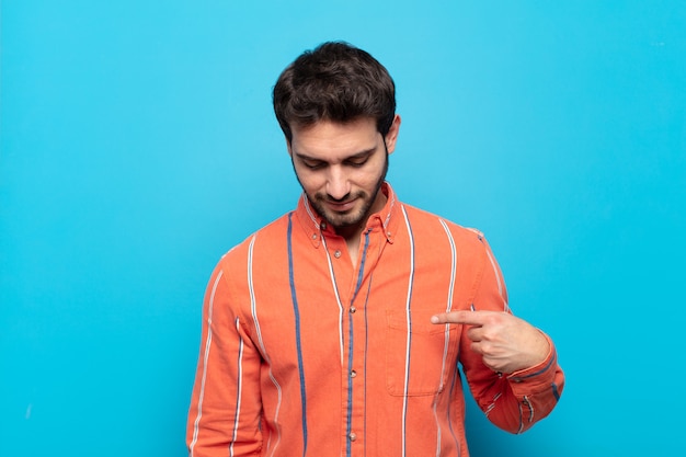 Young handsome man smiling cheerfully and casually, looking downwards and pointing to chest