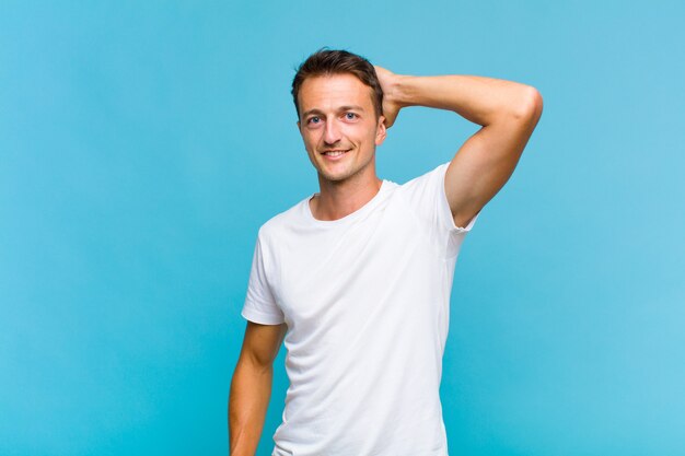 Young handsome man smiling cheerfully and casually, taking hand to head with a positive, happy and confident look