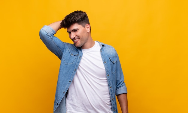 Young handsome man smiling cheerfully and casually, taking hand to head with a positive