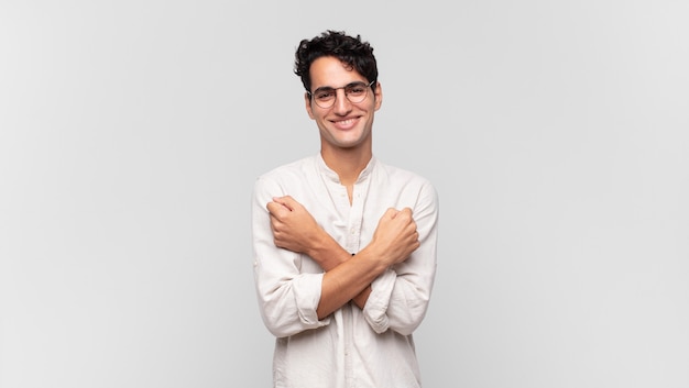 Young handsome man smiling cheerfully and celebrating, with fists clenched and arms crossed, feeling happy and positive