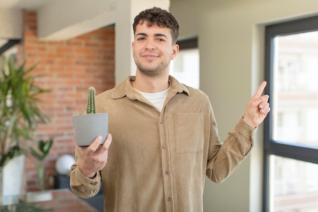 Foto giovane uomo bello che sorride allegramente sentendosi felice e indicando il concetto di pianta di cactus laterale