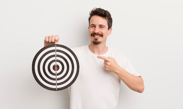 Young handsome man smiling cheerfully feeling happy and pointing to the side dart target concept