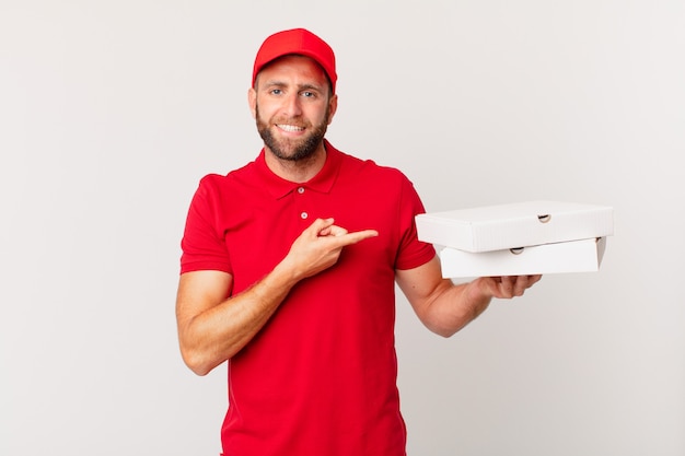 young handsome man smiling cheerfully, feeling happy and pointing to the side. pizza delivering concept