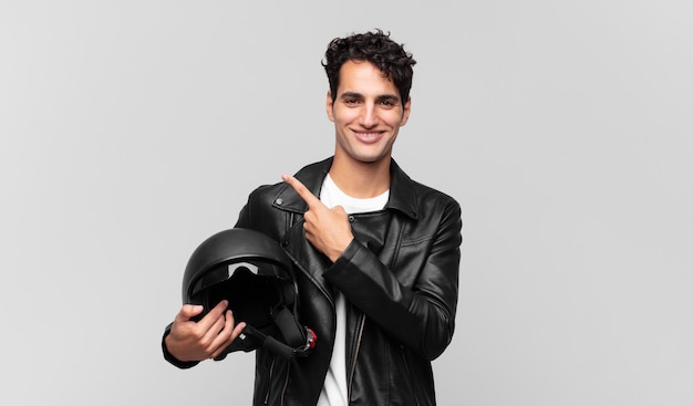 Young handsome man smiling cheerfully, feeling happy and pointing to the side and upwards, showing object in copy space. motorbike rider concept