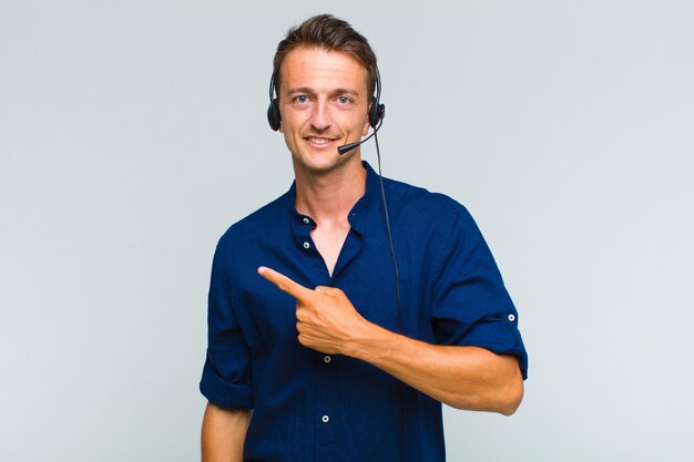 Photo young handsome man smiling cheerfully, feeling happy and pointing to the side and upwards, showing object in copy space