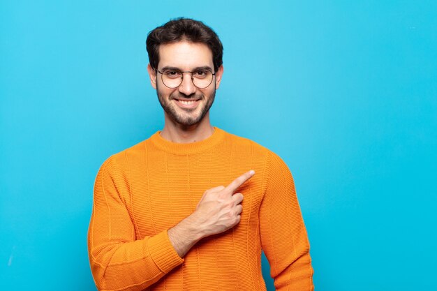 Young handsome man smiling cheerfully, feeling happy and pointing to the side and upwards, showing object in copy space