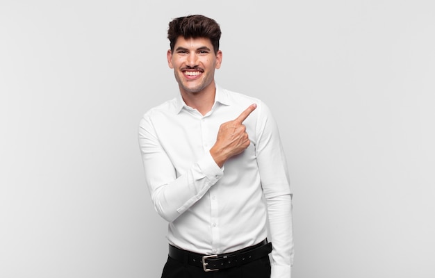 Young handsome man smiling cheerfully, feeling happy and pointing to the side and upwards, showing object in copy space