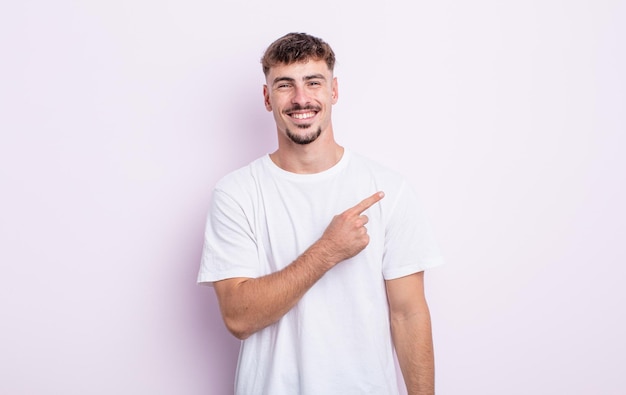 Young handsome man smiling cheerfully, feeling happy and pointing to the side and upwards, showing object in copy space