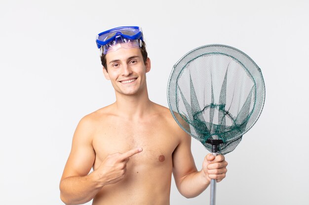 Young handsome man smiling cheerfully, feeling happy and pointing to the side with goggles and a fishing net