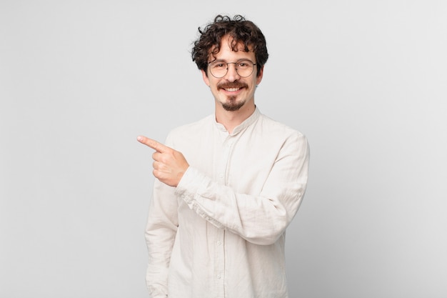 Young handsome man smiling cheerfully, feeling happy and pointing to the side