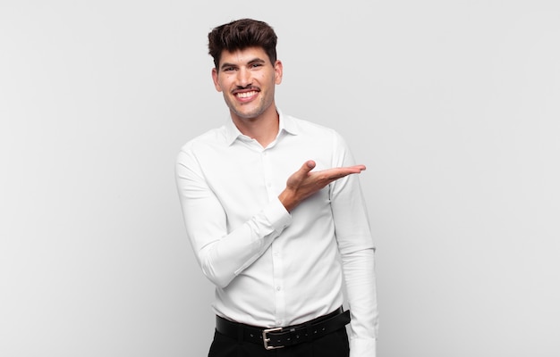 Young handsome man smiling cheerfully, feeling happy and showing a concept in copy space with palm of hand