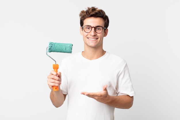 Young handsome man smiling cheerfully, feeling happy and showing a concept and holding a roller paint