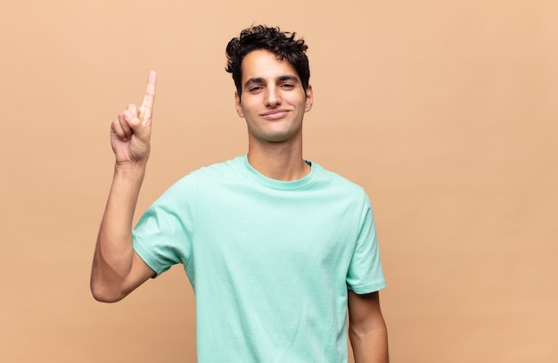 Young handsome man smiling cheerfully and happily, pointing upwards with one hand to copy space