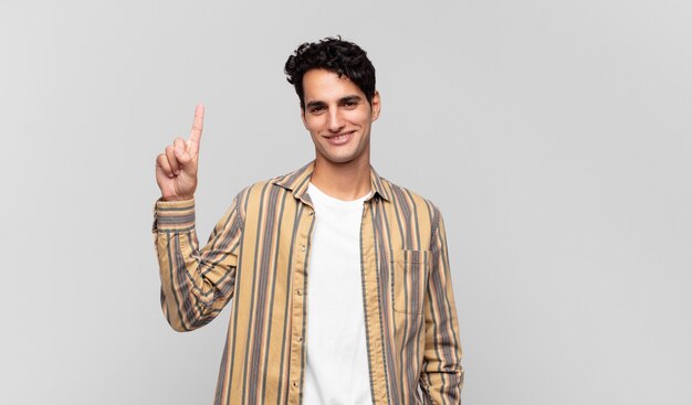 Young handsome man smiling cheerfully and happily, pointing upwards with one hand to copy space