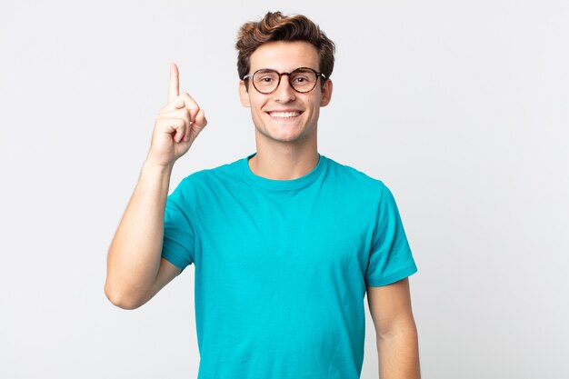 young handsome man smiling cheerfully and happily, pointing upwards with one hand to copy space