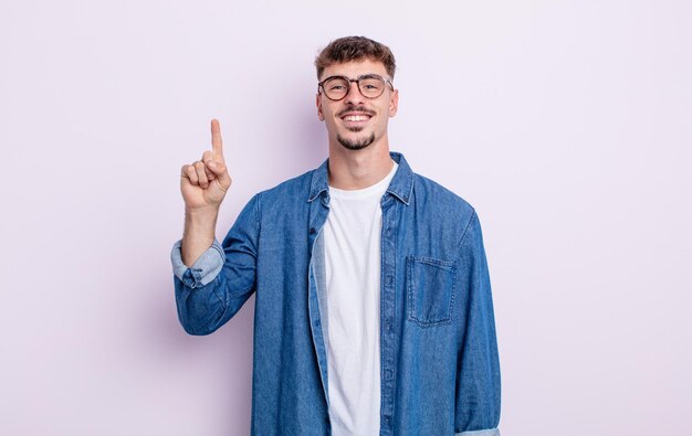 Young handsome man smiling cheerfully and happily pointing upwards with one hand to copy space