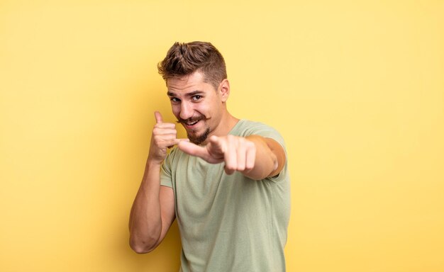 Young handsome man smiling cheerfully and pointing to camera while making a call you later gesture, talking on phone. strange moustache concept