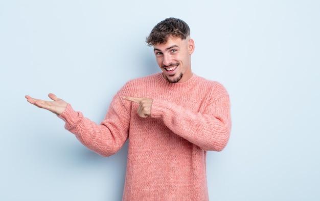 Young handsome man smiling cheerfully and pointing to copy space on palm on the side showing or advertising an object