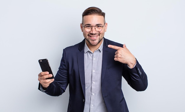 Young handsome man smiling confidently pointing to own broad smile business and smartphone concept