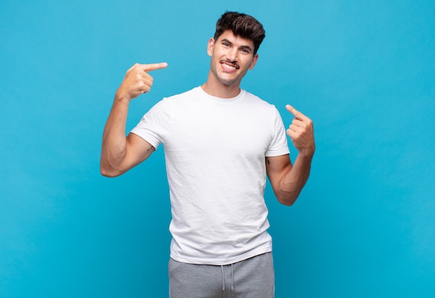 Young handsome man smiling confidently pointing to own broad smile, positive, relaxed, satisfied attitude