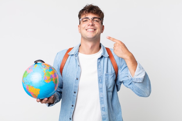 Giovane uomo bello che sorride con sicurezza indicando il proprio ampio sorriso. studente con in mano una mappa del globo