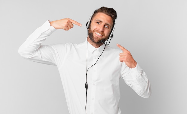 Young handsome man smiling confidently pointing to own broad smile. telemarketing concept