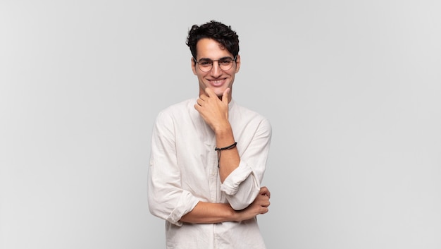 Young handsome man smiling, enjoying life, feeling happy, friendly, satisfied and carefree with hand on chin