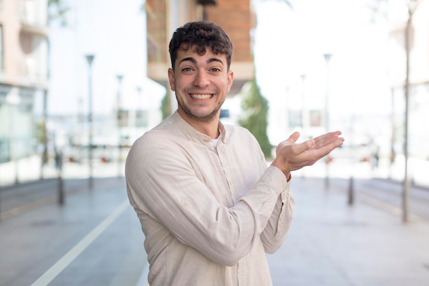 Photo young handsome man smiling, feeling confident, successful and happy, showing concept or idea on copy space on the side