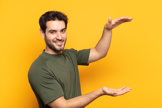 Young handsome man smiling, feeling happy, positive and satisfied, holding or showing object or concept on copy space