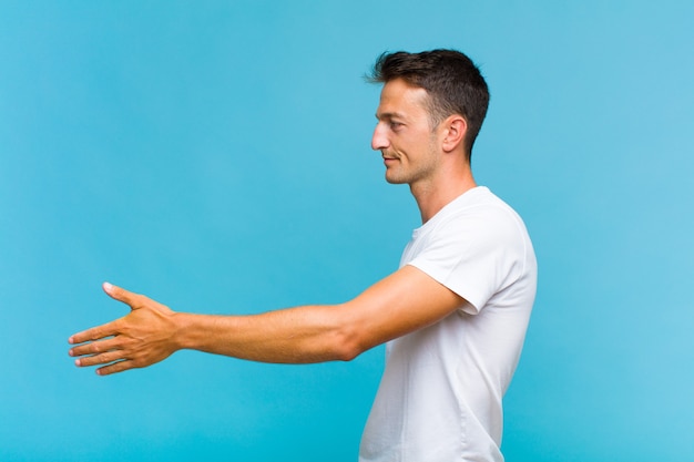 Giovane uomo bello sorridente, salutandoti e offrendoti una stretta di mano per chiudere un affare di successo, concetto di cooperazione