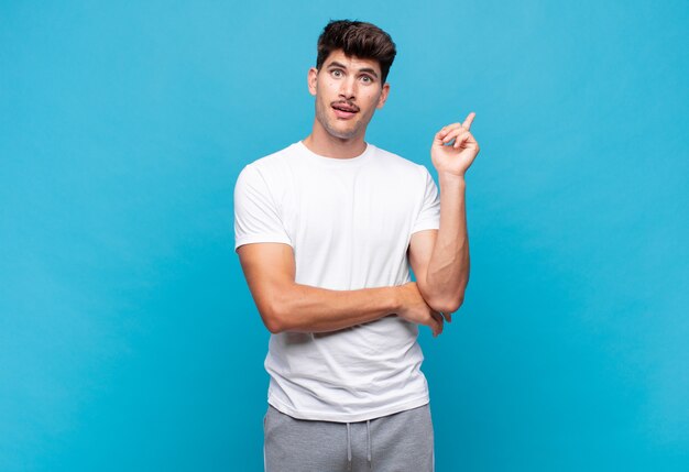 Young handsome man smiling happily and looking sideways, wondering, thinking or having an idea