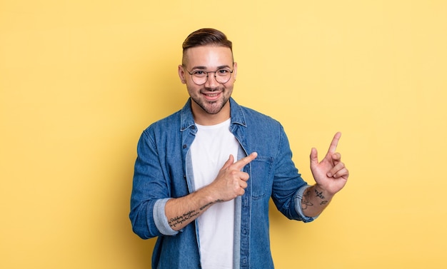 Young handsome man smiling happily and pointing to side and upwards with both hands showing object in copy space