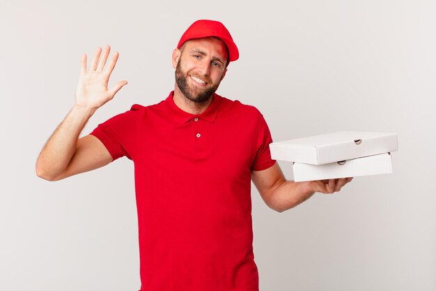 Foto giovane bell'uomo che sorride felicemente, agitando la mano, accogliendoti e salutandoti. concetto di consegna della pizza