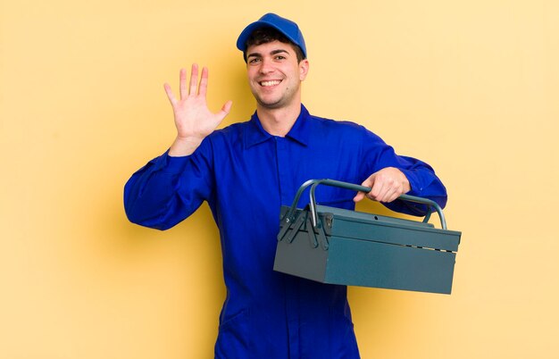 Young handsome man smiling happily waving hand welcoming and greeting you plumber concept