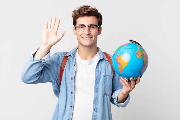 Young handsome man smiling happily, waving hand, welcoming and greeting you. student holding a world globe map