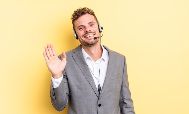 Giovane bell'uomo che sorride felicemente, agitando la mano, accogliendoti e salutandoti. concetto di telemarketing