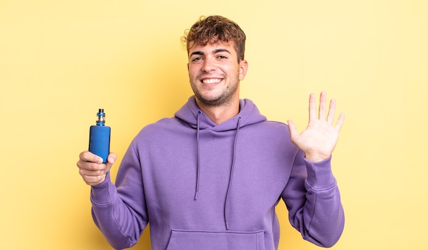 Young handsome man smiling happily, waving hand, welcoming and greeting you. vaporizer concept