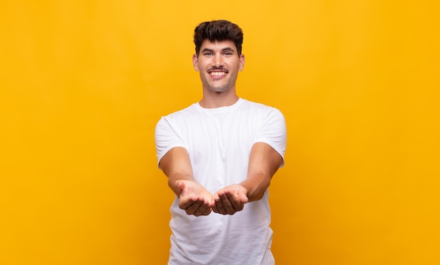 Young handsome man smiling happily with friendly, confident, positive look, offering and showing an object or concept