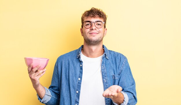 Giovane uomo bello che sorride felicemente con amichevole e offrendo e mostrando un concetto. concetto di ciotola vuota