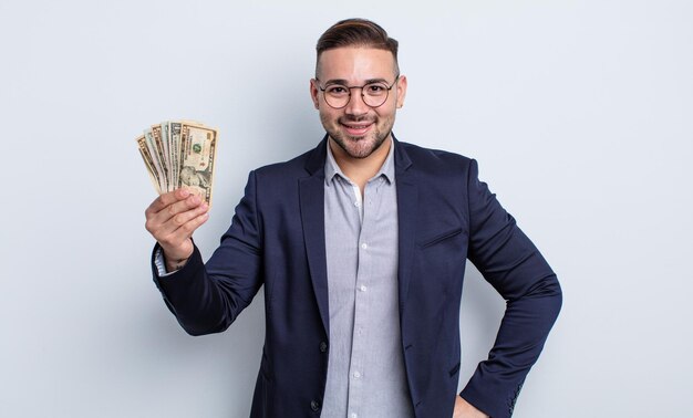 Young handsome man smiling happily with a hand on hip and confident. dollar banknotes concept