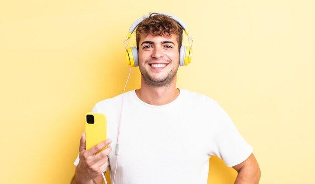 Young handsome man smiling happily with a hand on hip and confident headphones and smartphone concept