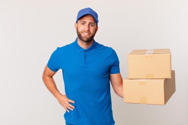 Young handsome man smiling happily with a hand on hip and confident. package delivering concept