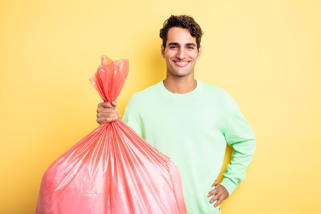 Young handsome man smiling happily with a hand on hip and confident trash bag concept