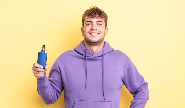 Young handsome man smiling happily with a hand on hip and confident. vaporizer concept