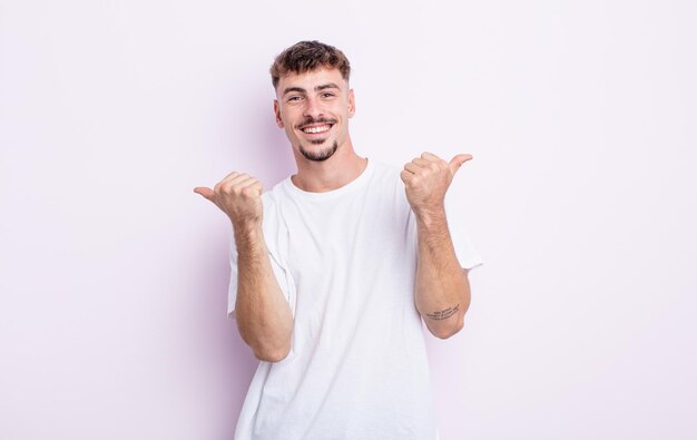 Young handsome man smiling joyfully and looking happy, feeling carefree and positive with both thumbs up