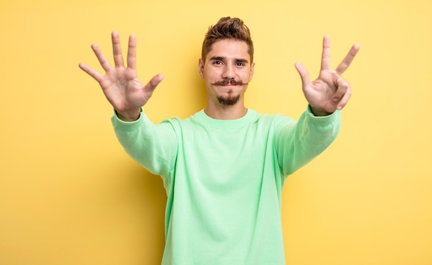 Young handsome man smiling and looking friendly, showing number eight or eighth with hand forward, counting down. strange moustache concept