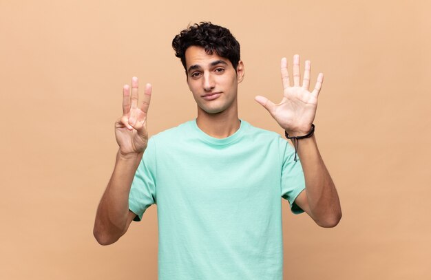 Giovane uomo bello sorridente e guardando amichevole, mostrando il numero otto o ottavo con la mano in avanti, conto alla rovescia