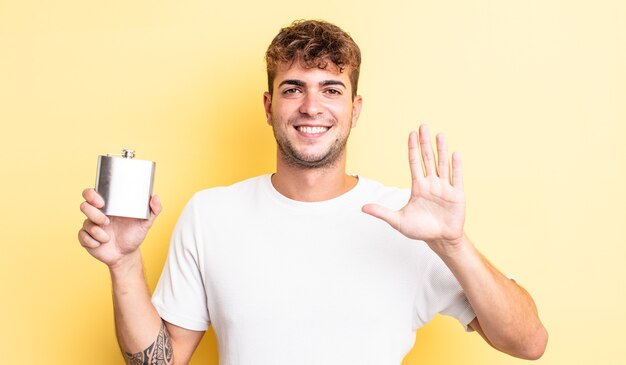 Young handsome man smiling and looking friendly, showing number five. alcohol flask concept