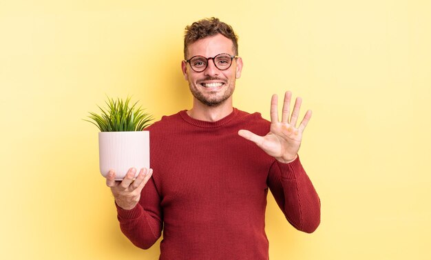 Young handsome man smiling and looking friendly, showing number five. decorative plant concept